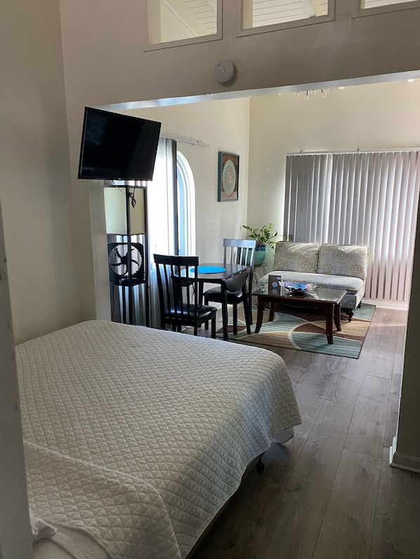 Un dormitorio con cama, televisor, escritorio con silla, sofá y ventana con cortinas.