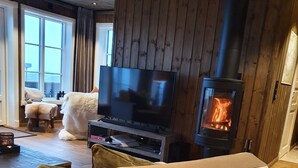 A cozy living room with a sofa, a flat-screen TV, and a wood-burning stove. - Ski-in/ski out at Lifjell . Perfect Place for Hikes in the Mountains (Vestfold og Telemark)