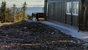 A wooden cabin with a sloped roof and a small porch, surrounded by a gravel driveway and a forested area. - Ski-in/ski out at Lifjell . Perfect Place for Hikes in the Mountains (Vestfold og Telemark)