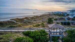 Vista costera con un paseo marítimo de madera, playa y casas frente al mar.