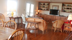 Un salon chaleureux avec un coin repas, des meubles en bois, un téléviseur et une bibliothèque.