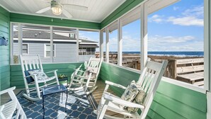 A covered porch with rocking chairs and a table, overlooking a beach. - Allston - 4 bedrooms, Oceanfront (Pawleys Island)