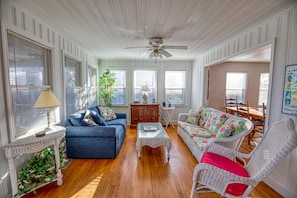 A spacious living room with a blue sofa, a wicker chair, a coffee table, and a ceiling fan.