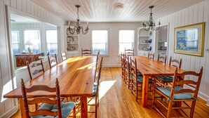 Comedor con una gran mesa y sillas de madera, paredes blancas con paneles y un candelabro.