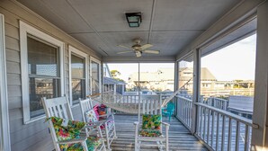 Una terraza de madera con mecedoras y una mesa, con vistas a una zona residencial.