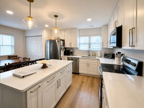 A modern kitchen with a central island, stainless steel appliances, white cabinetry, and pendant lighting. - Katinka II - Oceanside, 4 bedrooms (Pawleys Island)
