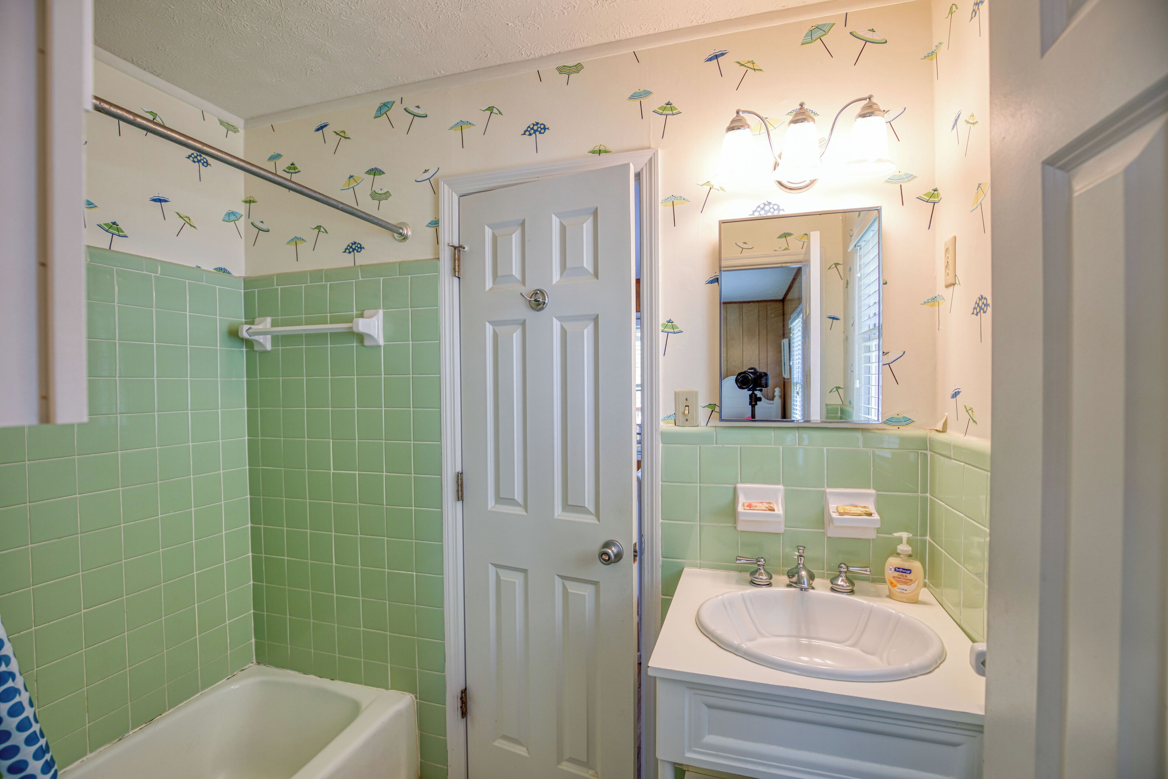 A bathroom with green tiles, a white bathtub, a white sink, and a mirror above the sink.