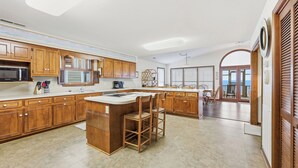 A spacious kitchen with wooden cabinets, a central island, and a view to the outside. - Schooler Shack - Oceanfront, 4 bedrooms (Pawleys Island)