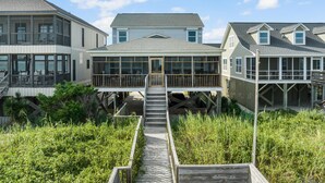 A coastal house with a covered porch, a deck, and a staircase leading to the entrance. - Schooler Shack - Oceanfront, 4 bedrooms (Pawleys Island)
