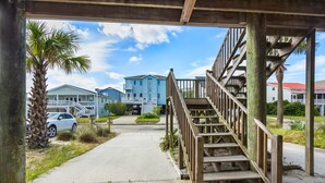 A wooden staircase leading to a covered area with a view of a residential street and houses. - Schooler Shack - Oceanfront, 4 bedrooms (Pawleys Island)