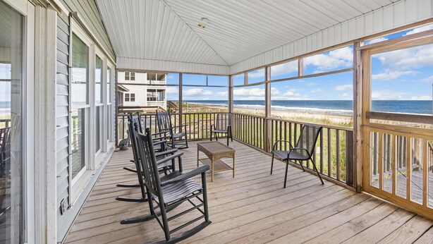A covered deck with wooden flooring, rocking chairs, a small table, and a view of the beach. - Schooler Shack - Oceanfront, 4 bedrooms (Pawleys Island)