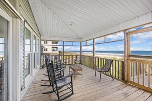 A covered deck with wooden flooring, rocking chairs, a small table, and a view of the beach. - Schooler Shack - Oceanfront, 4 bedrooms (Pawleys Island)