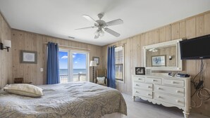 Een slaapkamer met een bed, een kaptafel, een plafondventilator en een televisie.