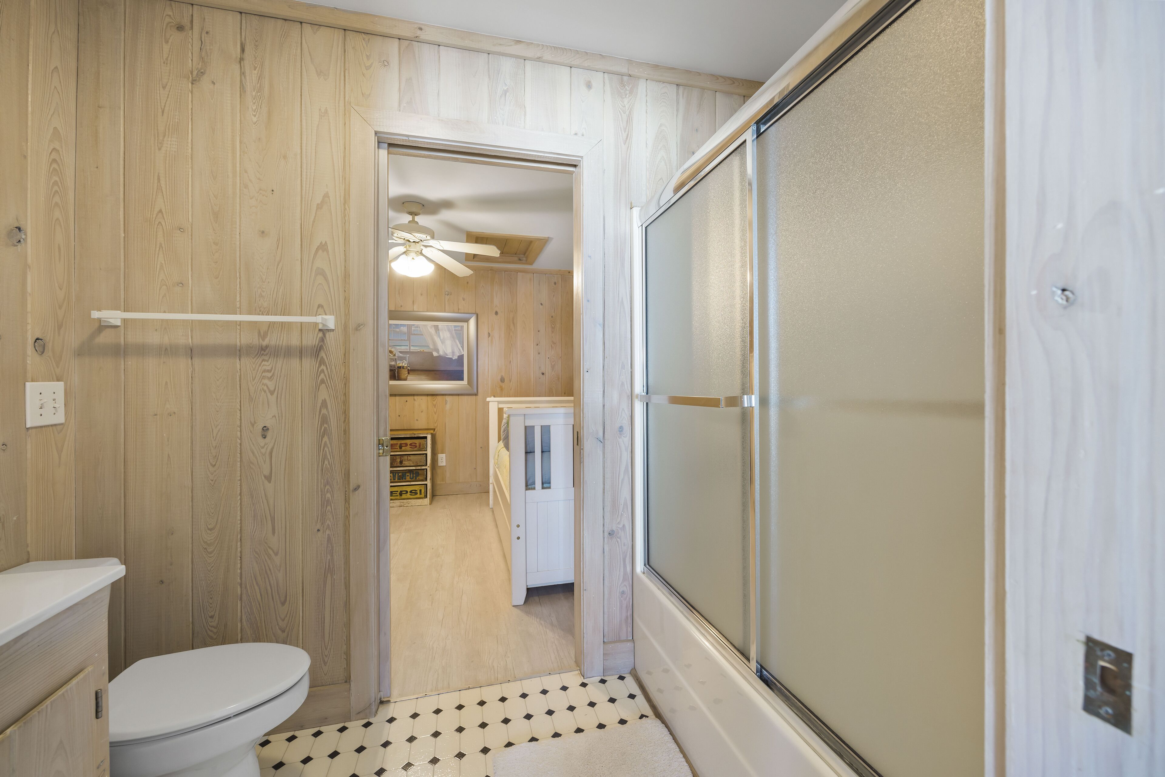 A bathroom with a wooden interior, a white toilet, a shower with a glass door, and a small window.