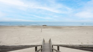 En træpromenade, der fører til en strand under en klar himmel.
