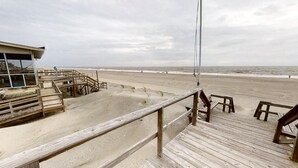 Uitzicht op het strand vanaf een houten terras, met een reddershutje en houten banken.