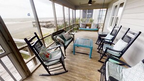 A covered outdoor seating area with a view of the beach, furnished with rocking chairs and a small table. - Sadler - Oceanfront, 6-Bedrooms (Pawleys Island)