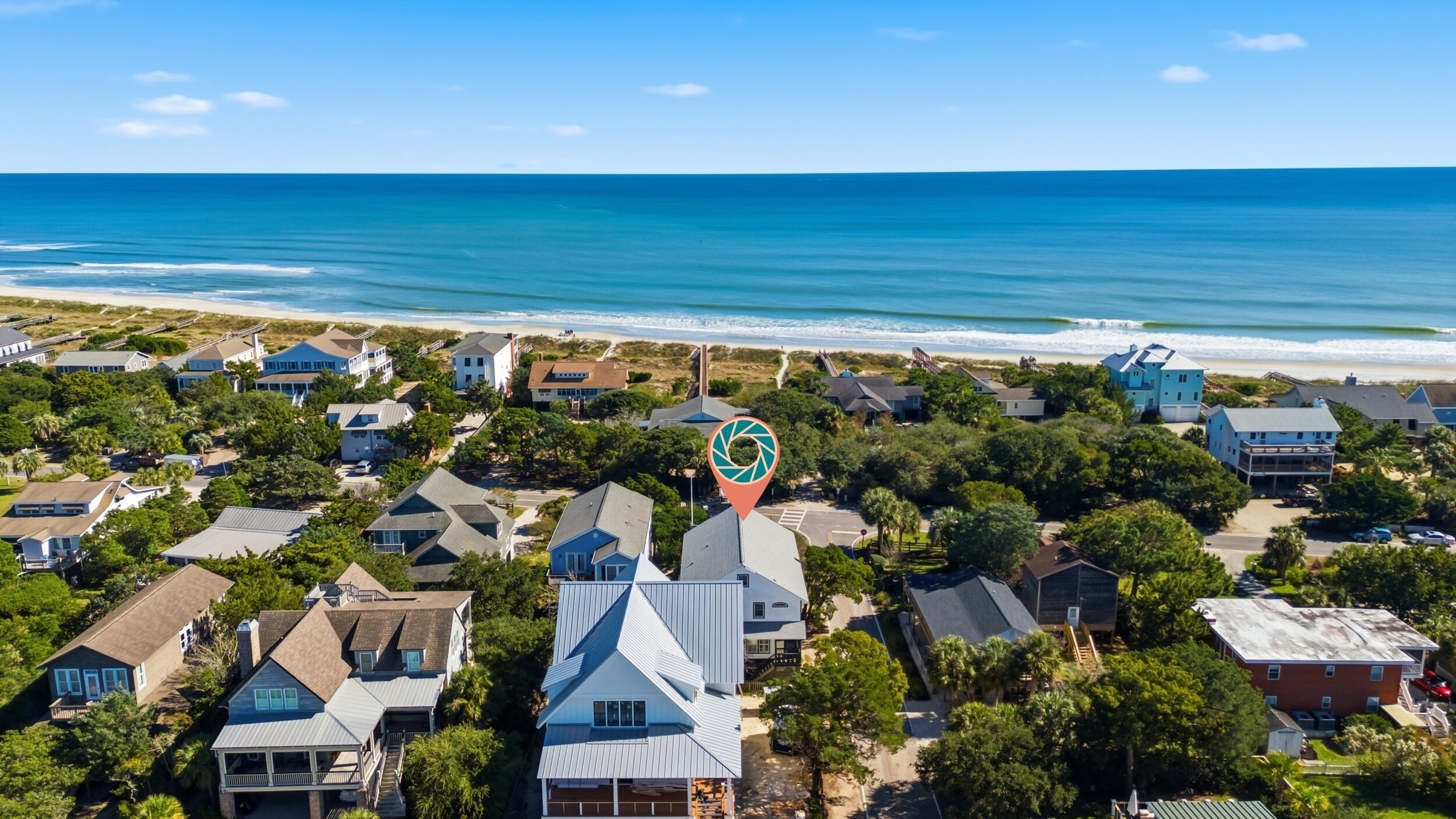An aerial view of a coastal residential area with houses, a beach, and a clear sky.