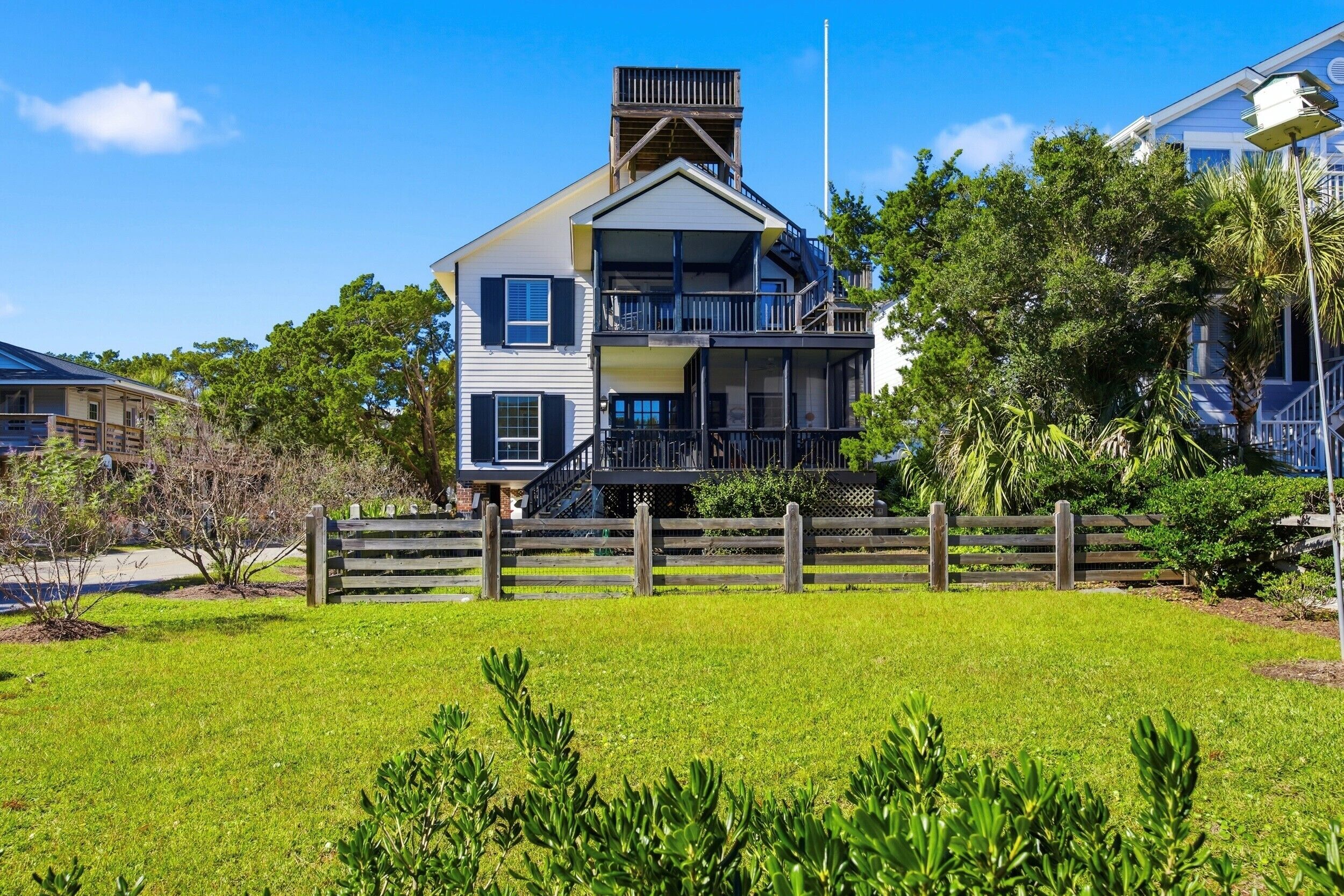 A two-story house with a balcony, surrounded by a wooden fence and lush greenery.
