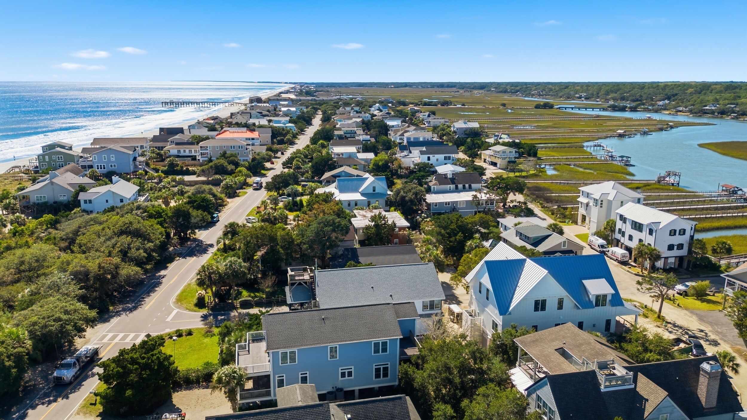 A coastal residential area with houses, a road, and a pier extending into the ocean.