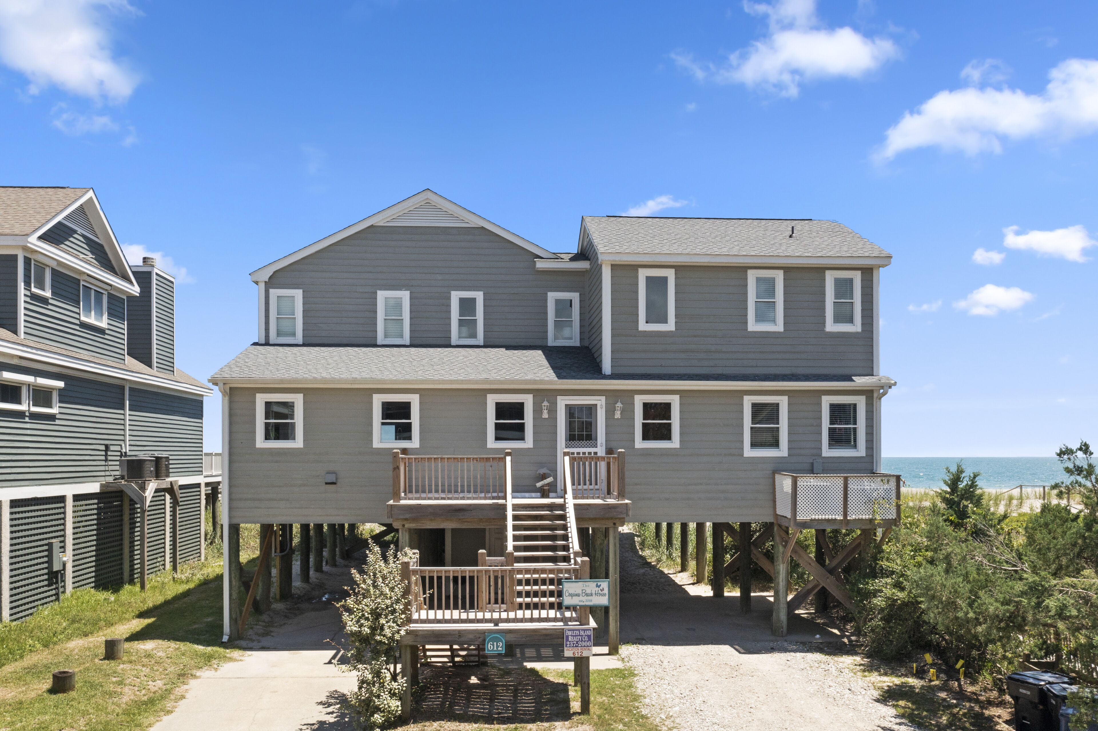 A two-story house with a balcony, a wooden deck, and a view of the ocean.