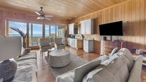 A spacious living area with a wooden ceiling, a large TV, and a view of the ocean.