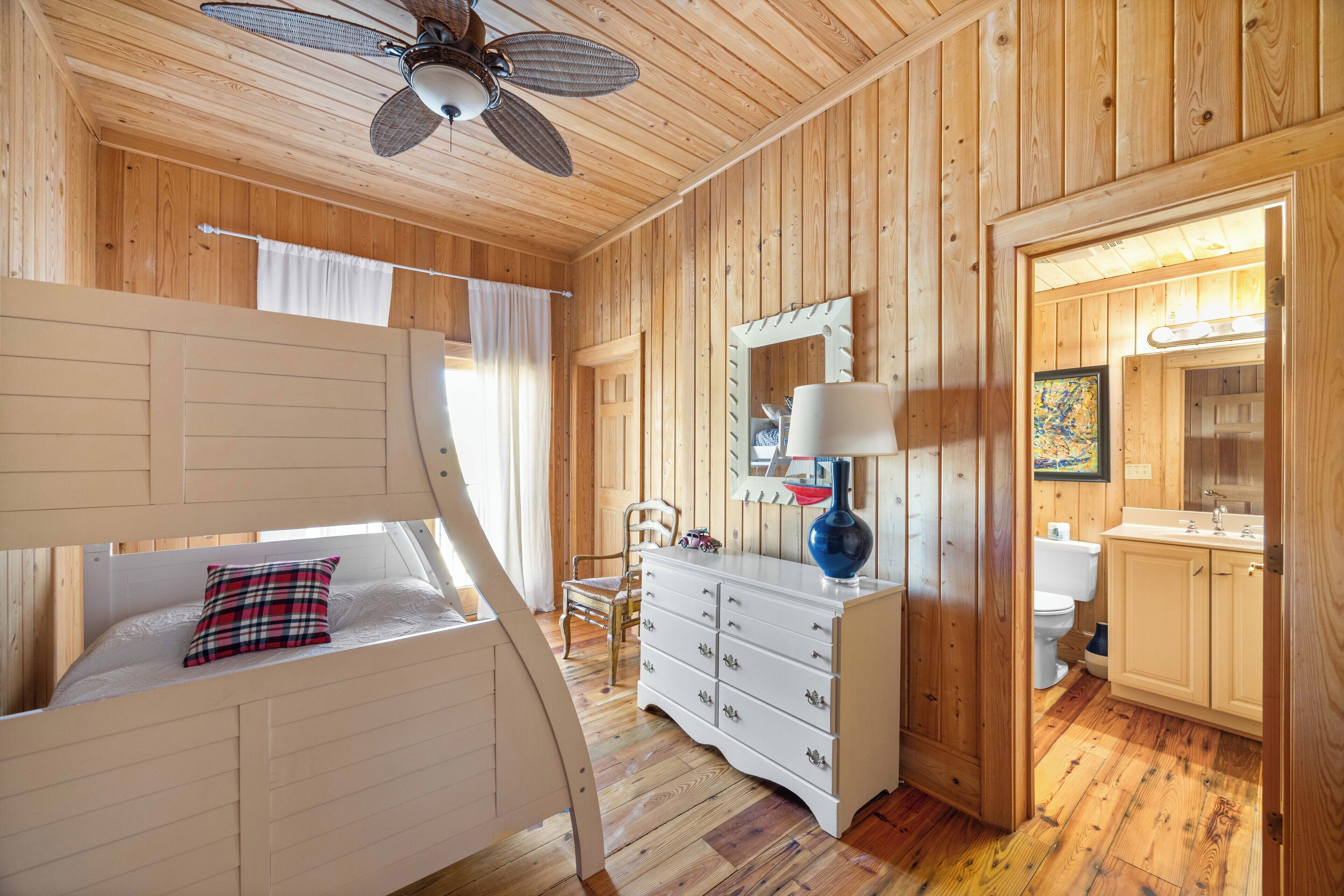 A wooden cabin room with a bunk bed, a dresser, a mirror, and a bathroom with a sink and toilet.