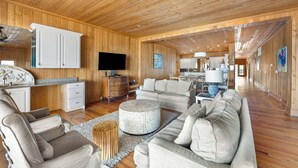 A spacious living area with wooden walls and floors, a large sofa, a coffee table, and a flat-screen TV.