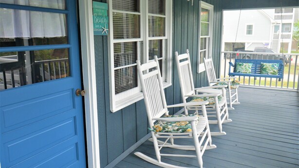 A porch with white rocking chairs and a blue door.