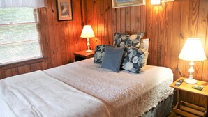 A wooden-paneled room with a bed, two bedside lamps, and a framed picture on the wall.