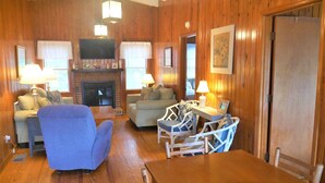 A cozy living room with wooden walls, a fireplace, a television, and a dining area with a table and chairs.