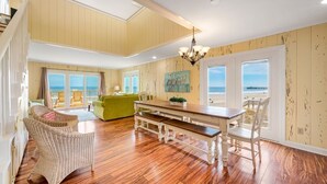 Un salón espacioso con suelo de madera, una mesa de comedor, sillas de mimbre y un sofá verde.