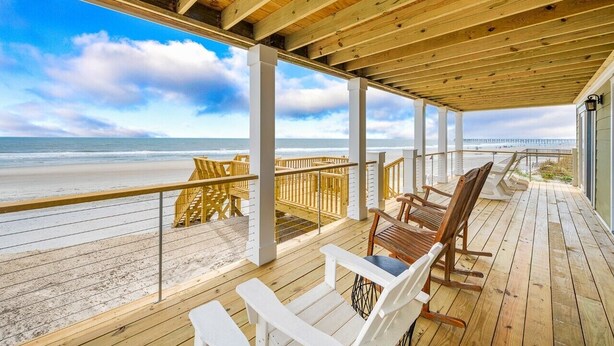 Una terraza de madera con sillas con vista a la playa.
