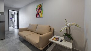 Una sala moderna con un sofá beige, una mesita auxiliar con un florero de flores blancas y un cuadro abstracto colorido en la pared.
