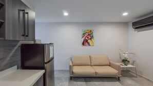 Una cocina moderna con un refrigerador, un sofá color beige y un cuadro colorido en la pared.