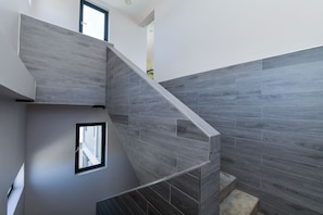 A modern staircase with grey wooden steps and walls, a small window, and a door leading to another room.