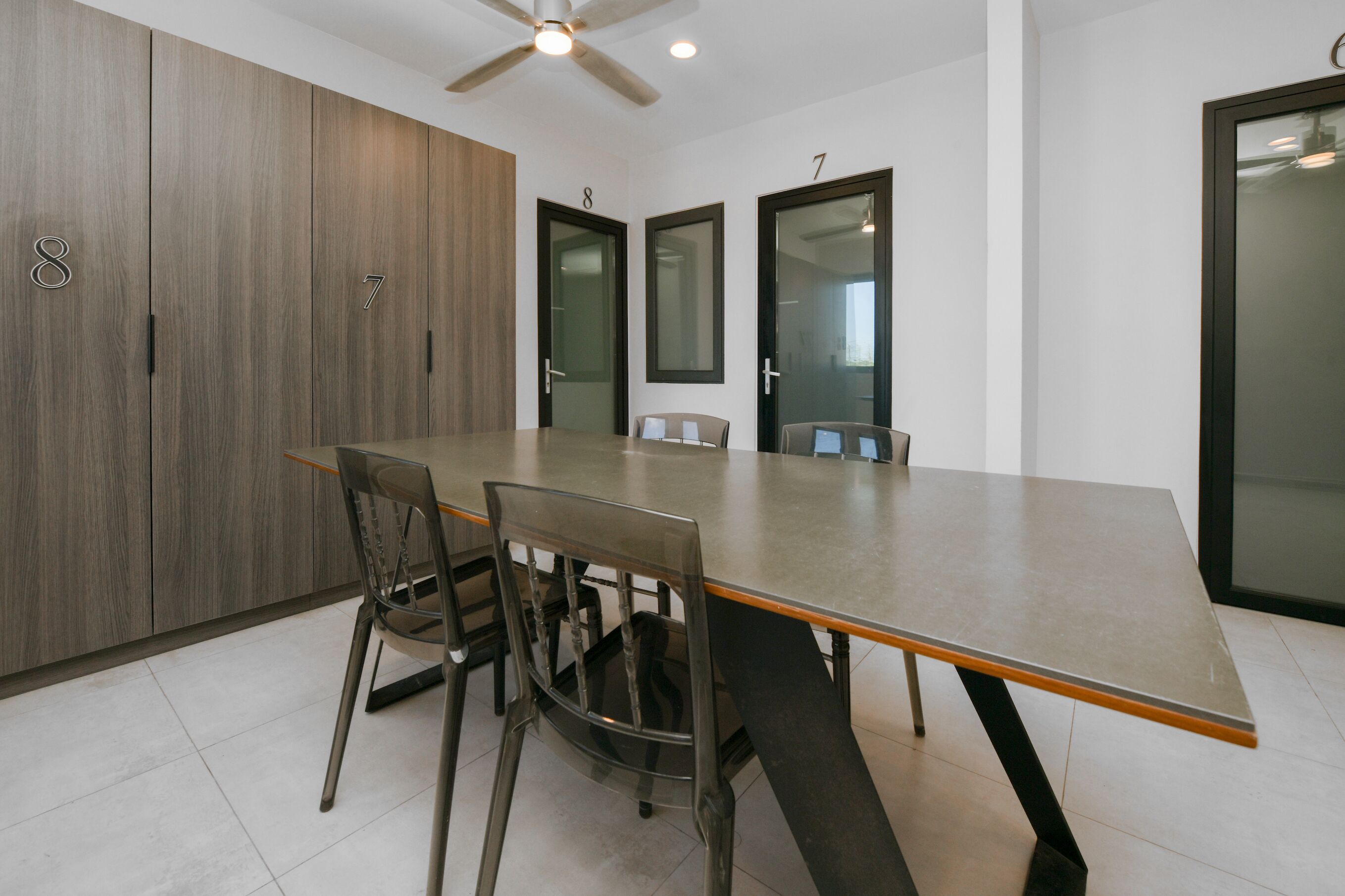 A modern dining area with a long table, four chairs, and a ceiling fan.