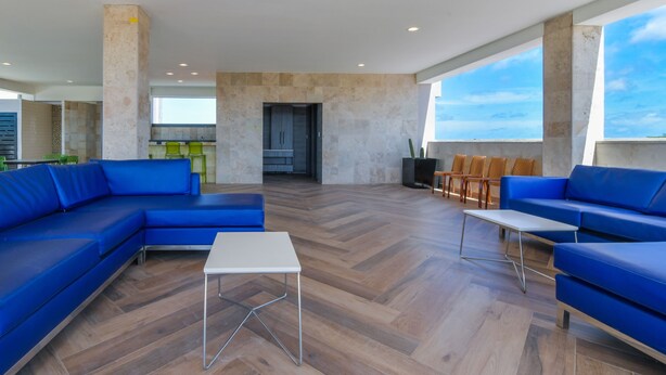 Un espacio habitable amplio con un sofá seccional azul grande, una mesa de centro blanca y una zona de estar con sillas de madera.