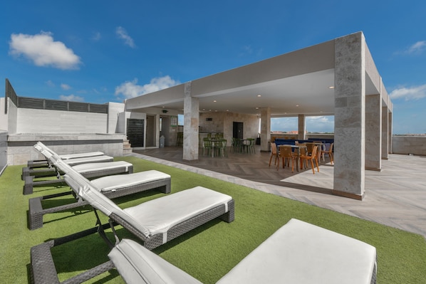 A rooftop terrace with sun loungers, a dining area, and a view of the city.