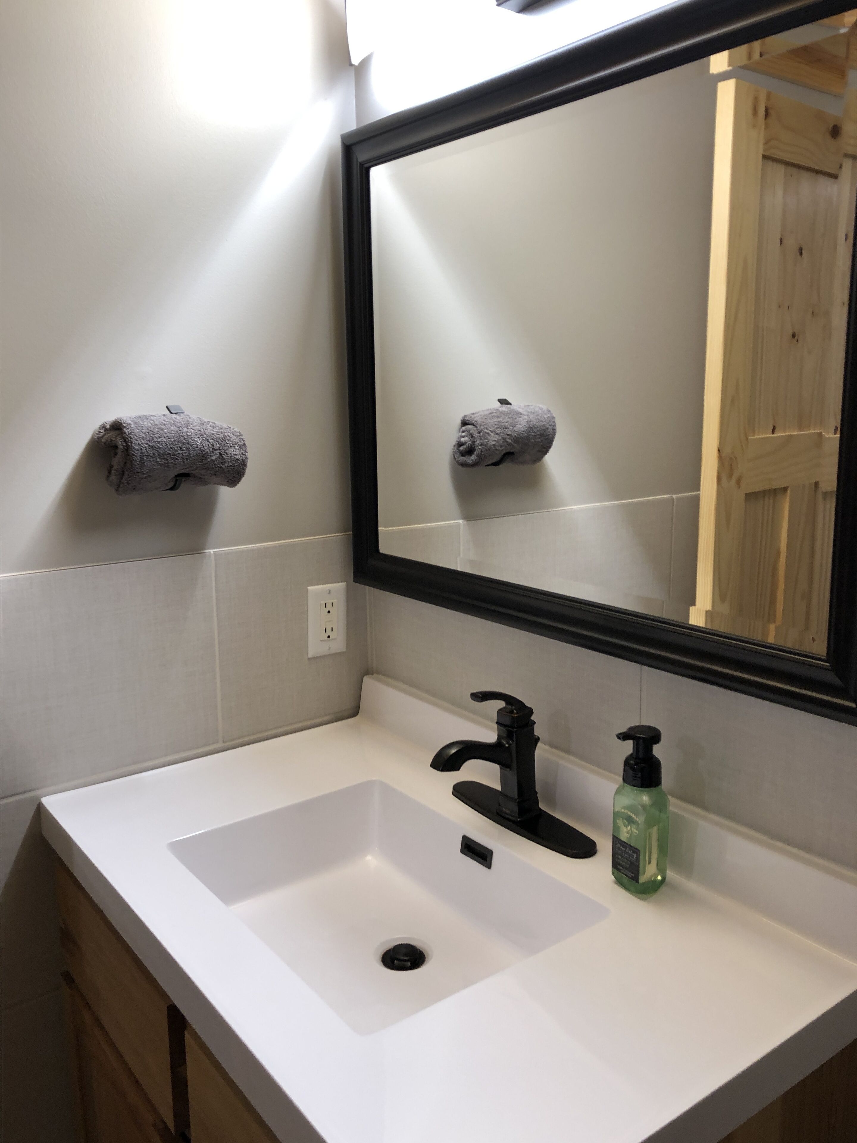 A bathroom with a white sink, black faucet, and a mirror with a black frame. There are two towels hanging on the wall.