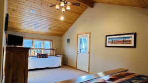 A bedroom with a wooden ceiling, a bed, a TV on a cabinet, and a window with a view of trees. - Mountain Chalet Tucked in Aspen Grove with Mountain Views (Angel Fire)