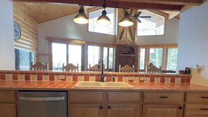 A kitchen with wooden cabinets, a built-in dishwasher, a large window, and a ceiling fan. - Mountain Chalet Tucked in Aspen Grove with Mountain Views (Angel Fire)