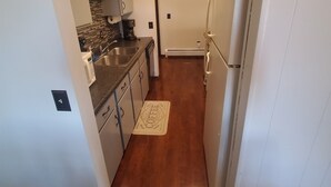 Una cocina compacta con armarios blancos, un lavamanos de acero inoxidable y un refrigerador blanco.