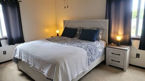 Ein ordentlich bezogenes Bett mit einem gemusterten Überwurf, zwei Nachttischlampen, einem Deckenventilator und einem Nachttisch mit Schubladen.