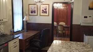Una cocina con encimera de granito, un escritorio de madera, una lámpara de araña y cuadros en la pared.