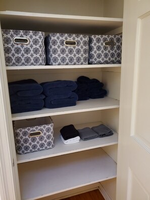 A closet with three shelves, each containing folded towels and storage boxes with a patterned design.