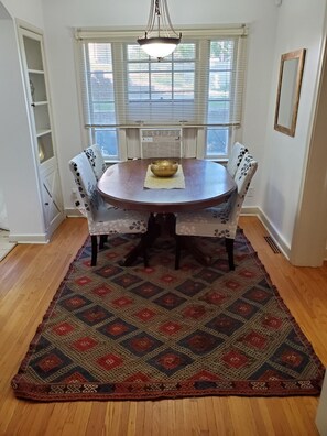 A dining area with a round table, two chairs, a decorative rug, and a window with blinds.