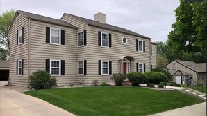 A two-story house with a symmetrical facade, a central entrance with a red door, and a well-maintained lawn. - Historic Mc Kennan Park Apt 5 (1 bed 1 bath) - KP220APT5 (Sioux Falls)
