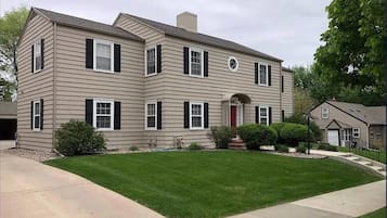 A two-story house with a symmetrical facade, a central entrance with a red door, and a well-maintained lawn.