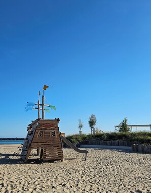 A wooden lifeguard tower with a slide on a sandy beach.